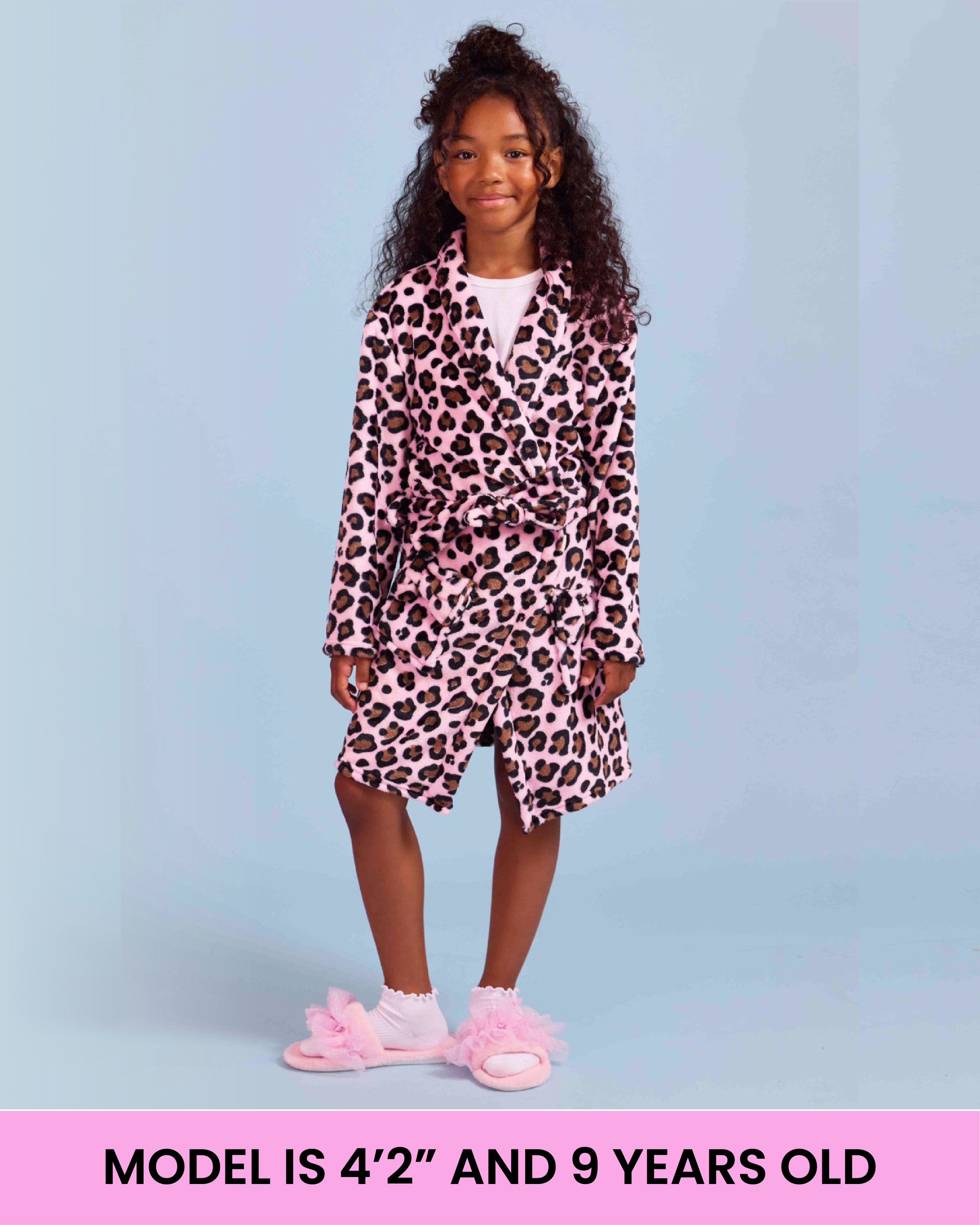 A young girl models a pink and black leopard print bathrobe against a light blue background. A pink banner at the bottom reads 'MODEL IS 4'2" AND 9 YEARS OLD'.