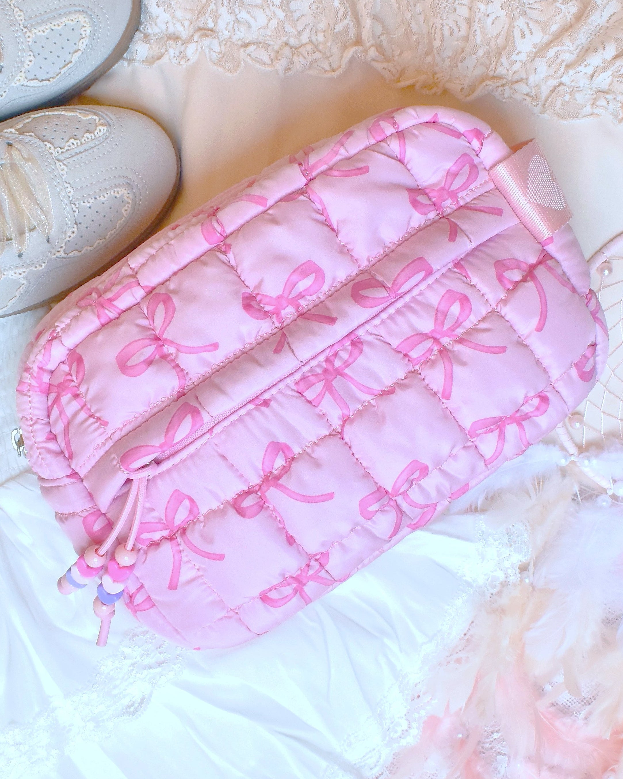 Photoshoot photo o a pink nylon quilted makeup pouch with a pink bow print, and beaded puller front zipper pocket