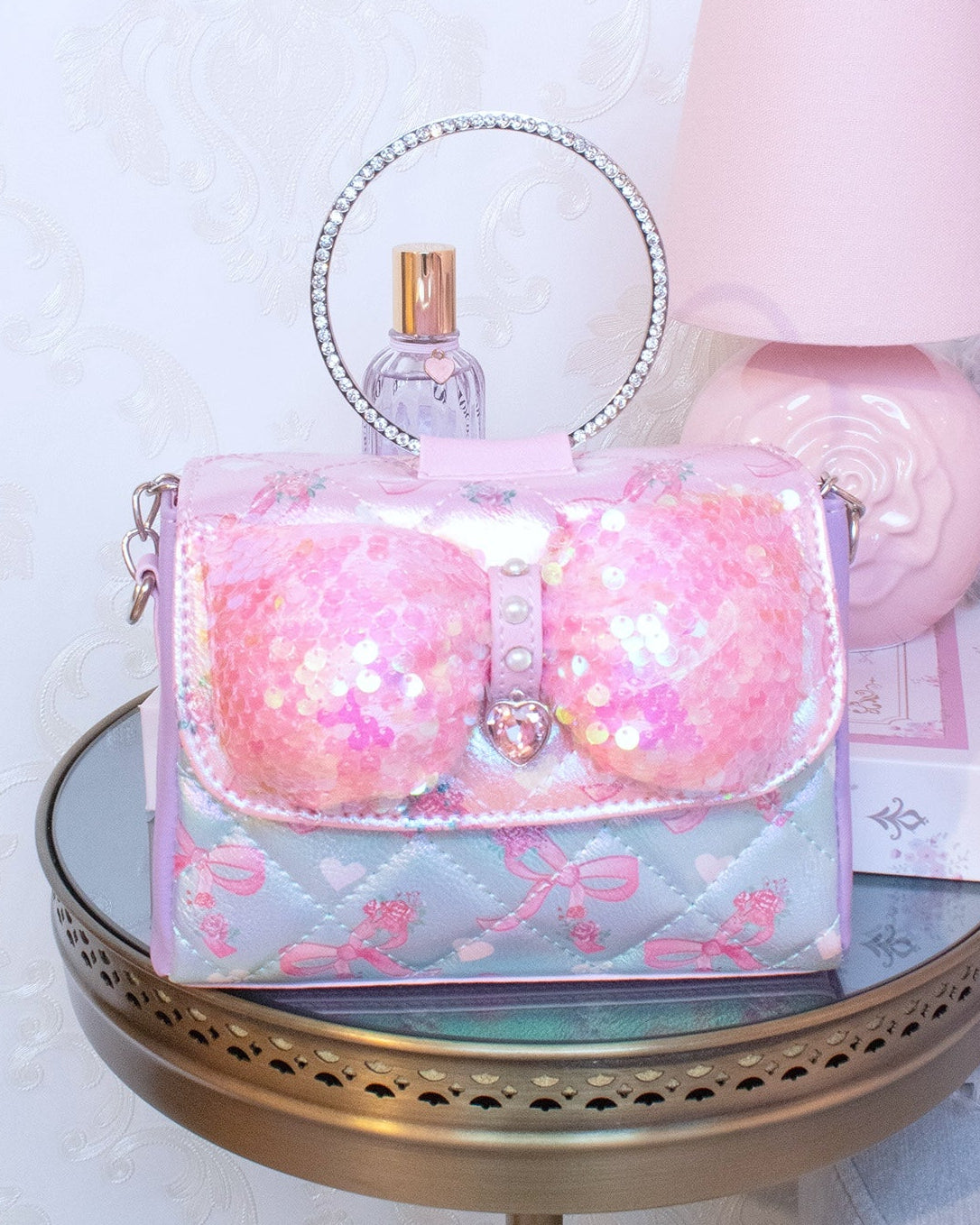 Lifestyle photo of a metallic color blocked mini bag with a round rhinestone handle and a large puffer sequins bow on the front flap