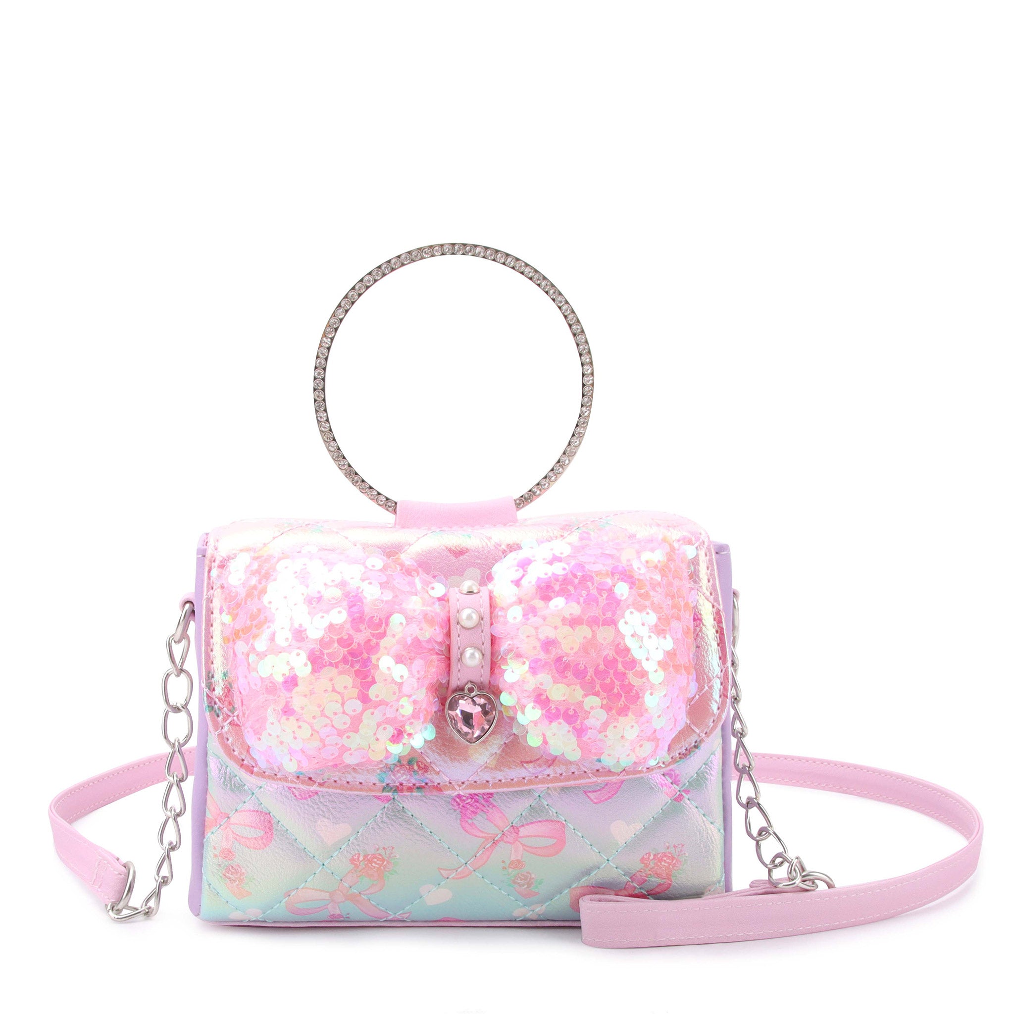 front view of a sequin & metallic bow printed flap front bag. topped with a rhinestone ring top handle & pearl & gem heart front closure