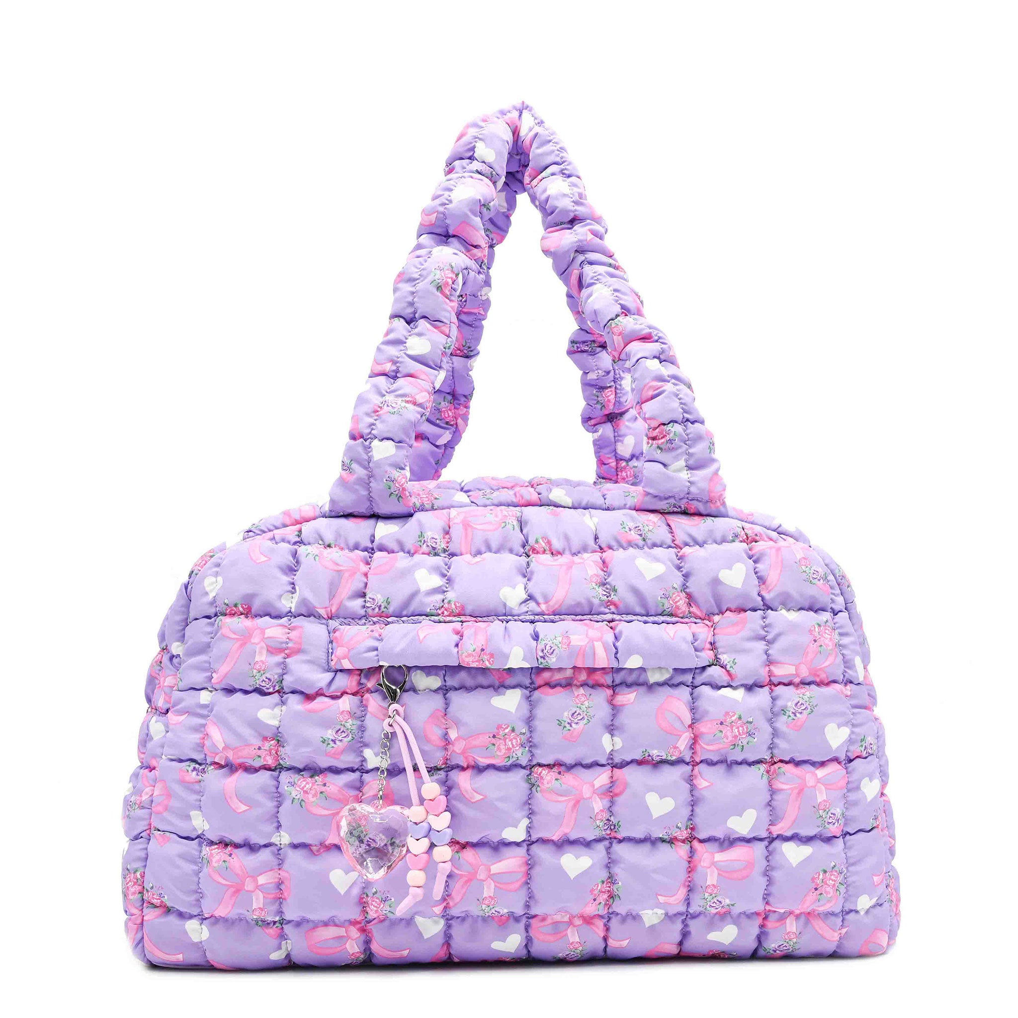 front facing view of a purple quilted scrunch medium sized duffe bag with a bow/floral/heart print and front zipper pocket with a beaded zipper and crystal heart charm