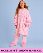 A young girl wearing a pink hooded pajama set with an allover bow pattern, standing against a light blue background. A pink banner at the bottom reads 'MODEL IS 4'5" AND 10 YEARS OLD'.
