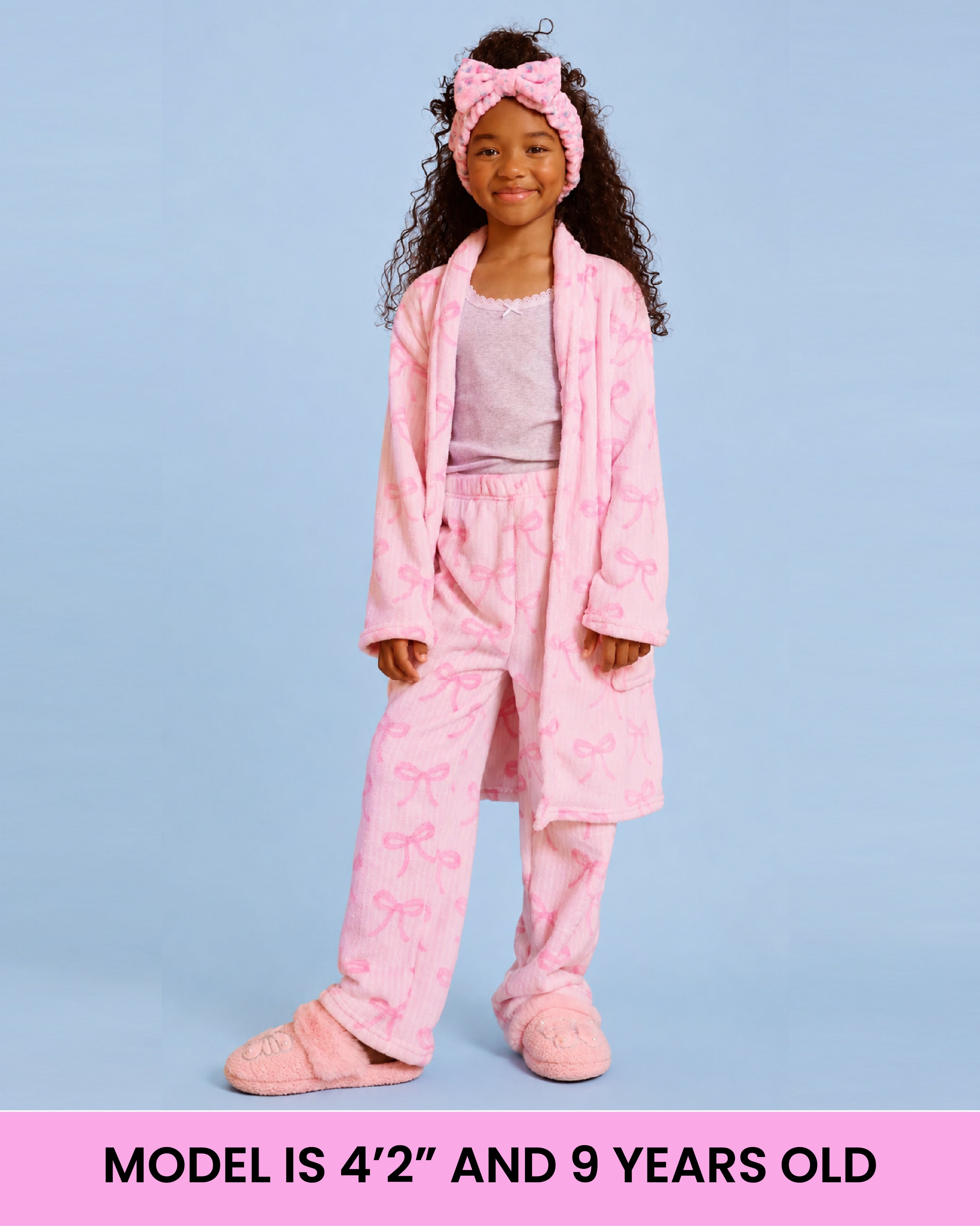A model wearing a pink striped bow bath robe in front of a light blue background with text that reads "model is 4'2" and 9 years old"