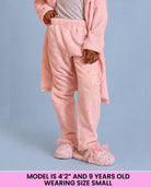 A child wearing pink plush pajama pants, standing against a light blue background. A pink text banner at the bottom reads: 'MODEL IS 4'2" AND 9 YEARS OLD WEARING SIZE SMALL'.
