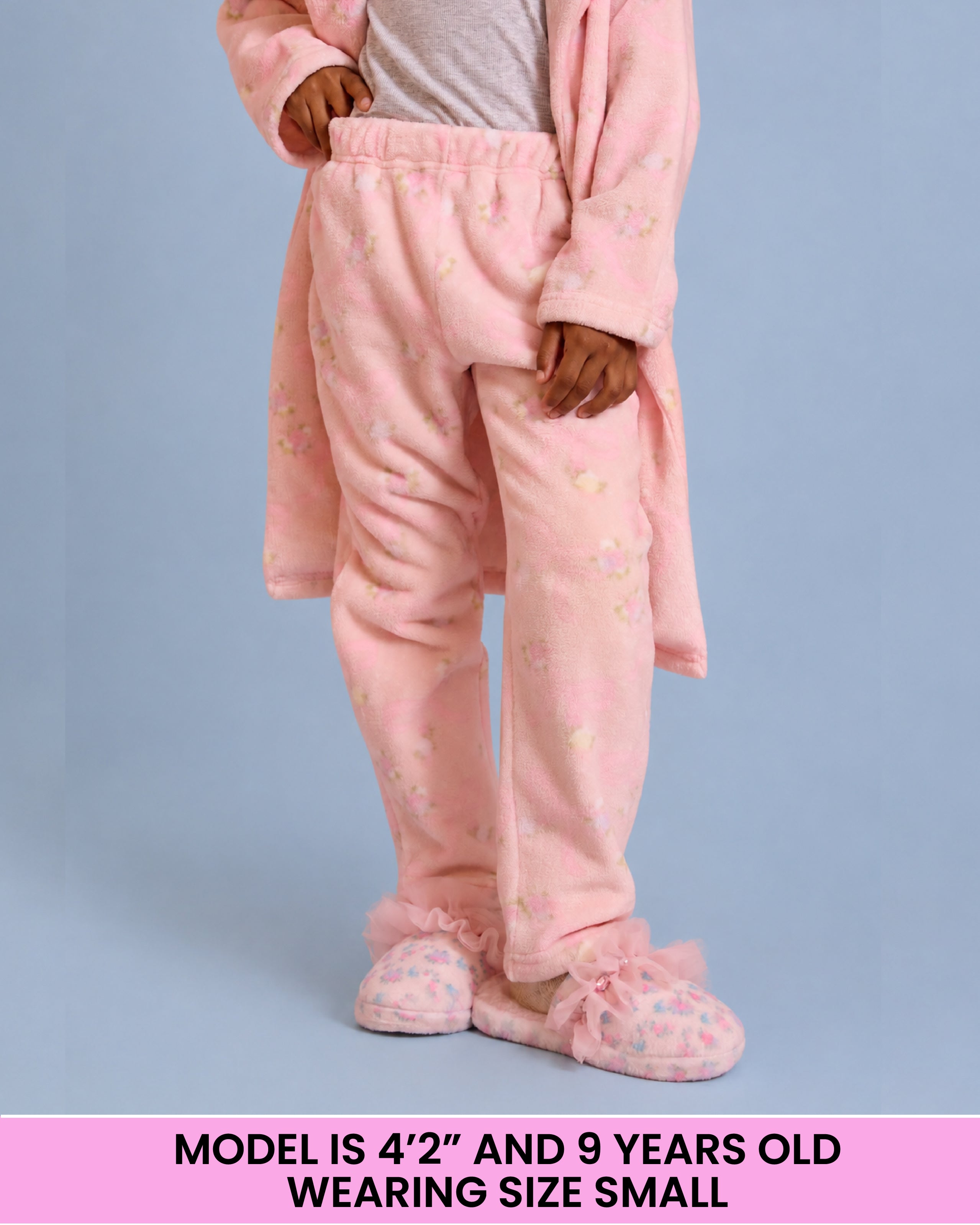 A child wearing pink plush pajama pants, standing against a light blue background. A pink text banner at the bottom reads: 'MODEL IS 4'2" AND 9 YEARS OLD WEARING SIZE SMALL'.