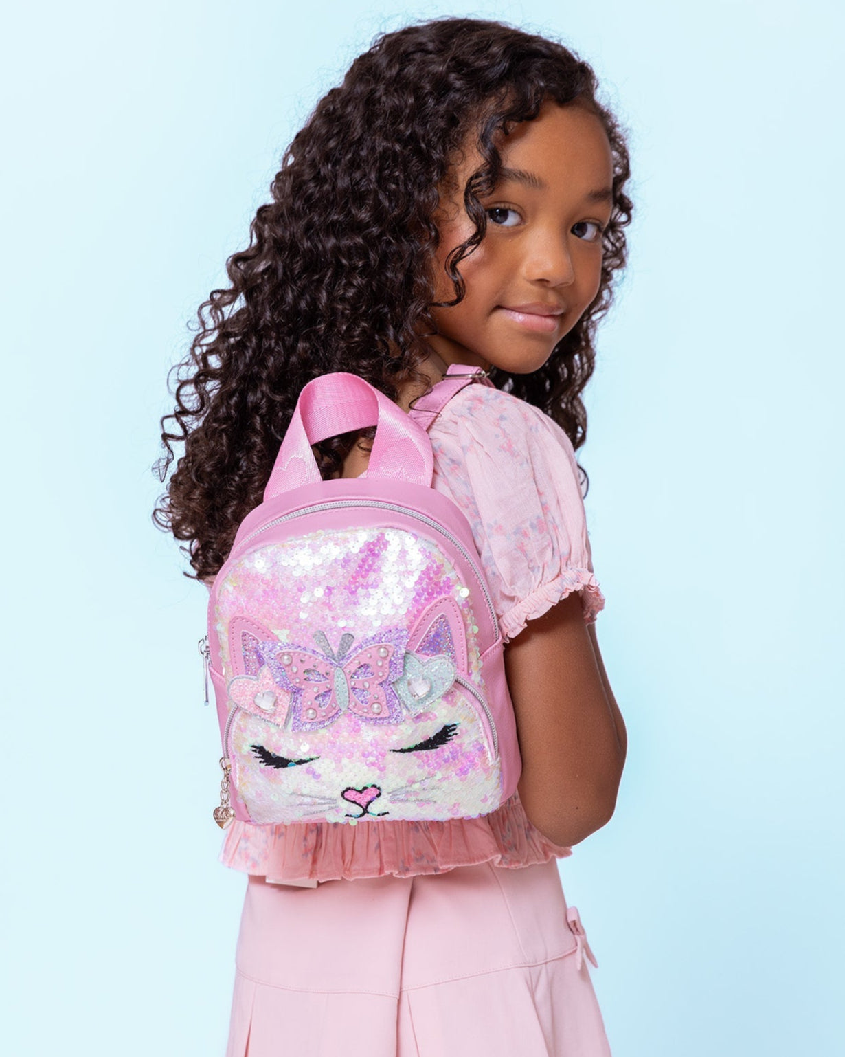 model wearing a sequin micro mini backpack with a kitty cat face on her shoulders
