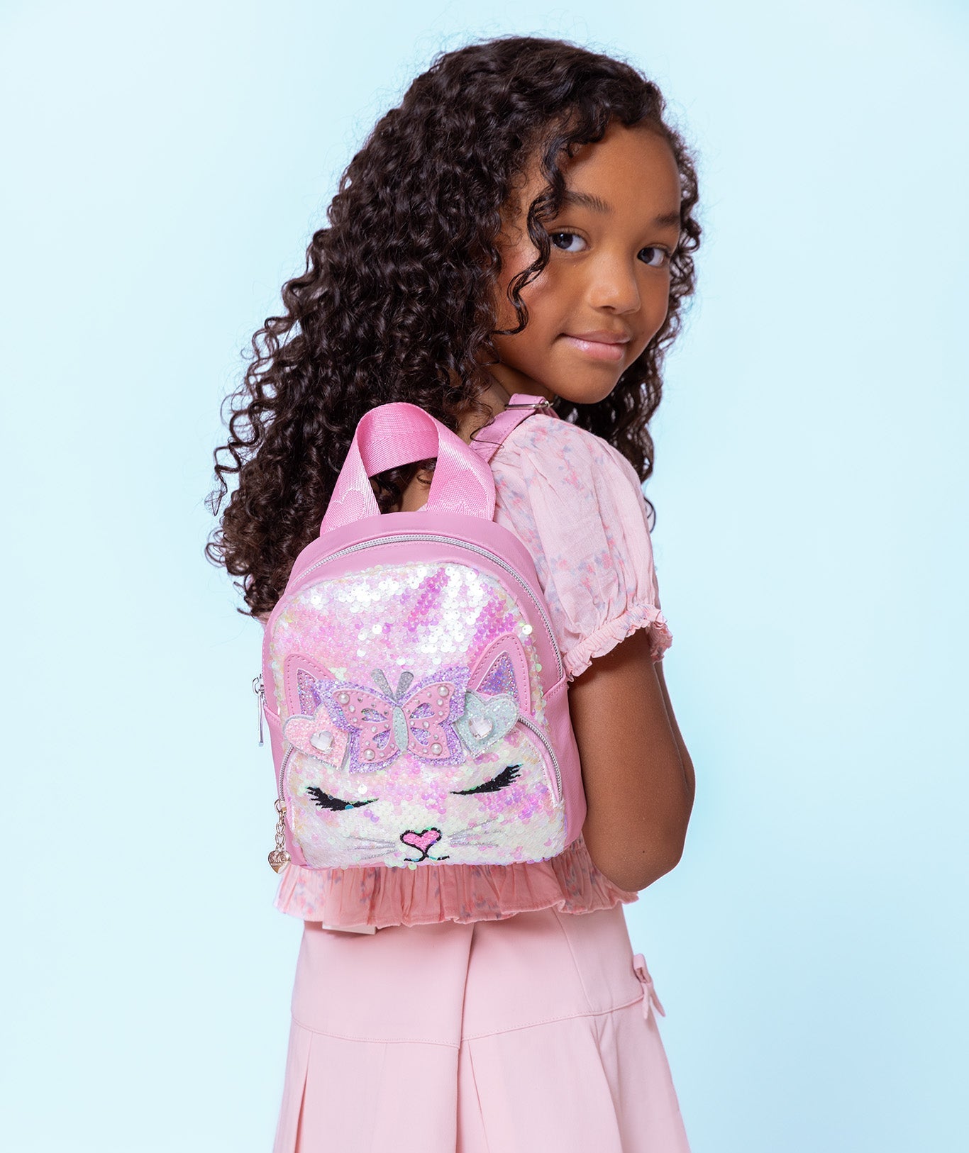 model wearing a sequin micro mini backpack with a kitty cat face on her shoulders
