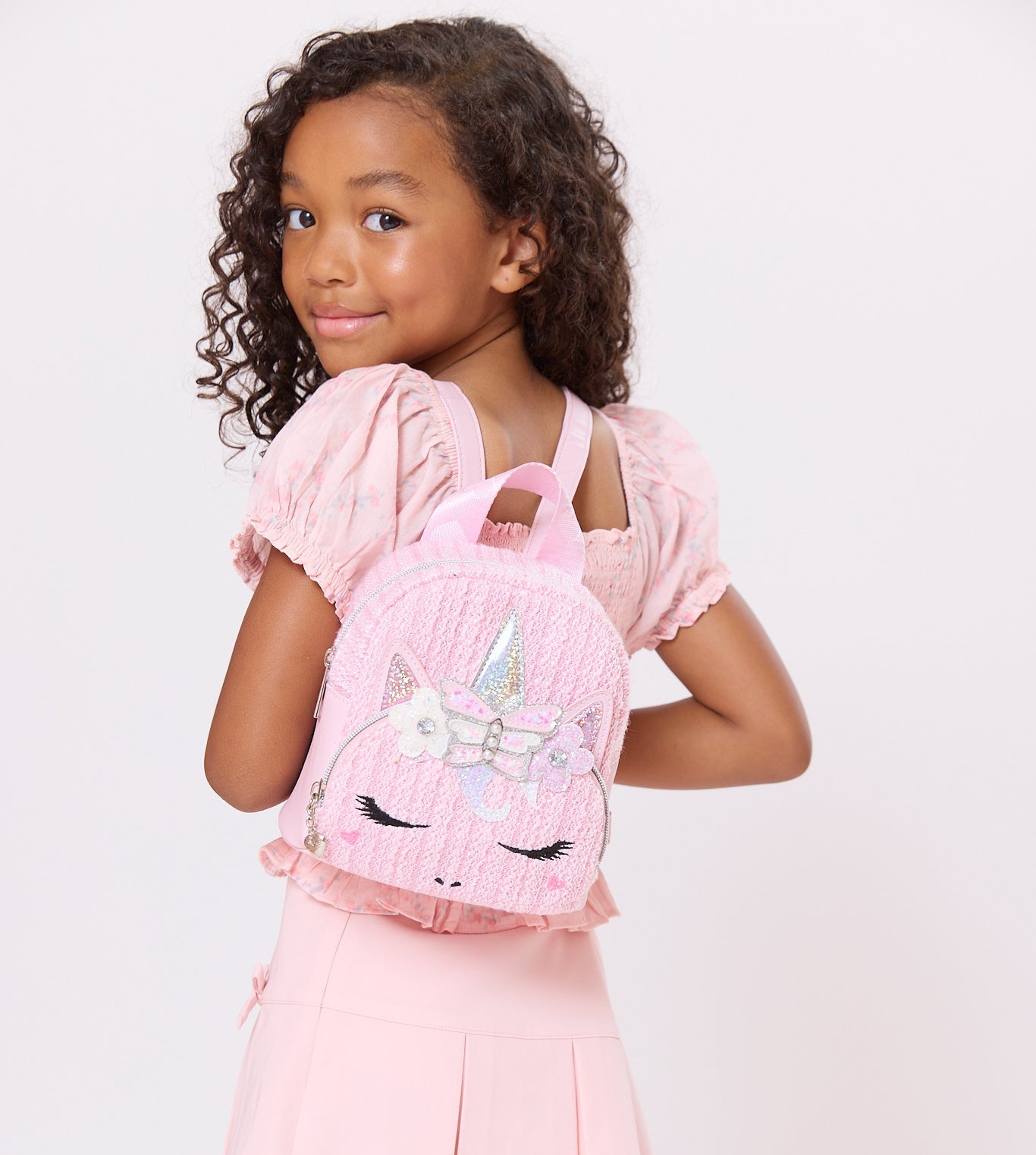model wearing pink woven micro mini backpack with unicorn face over her shoulders