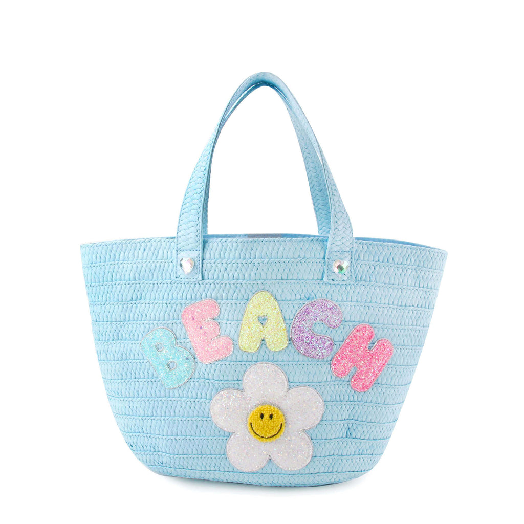 Front view of a blue straw beach tote with glitter bubble letters 'BEACH' and daisy appliqué