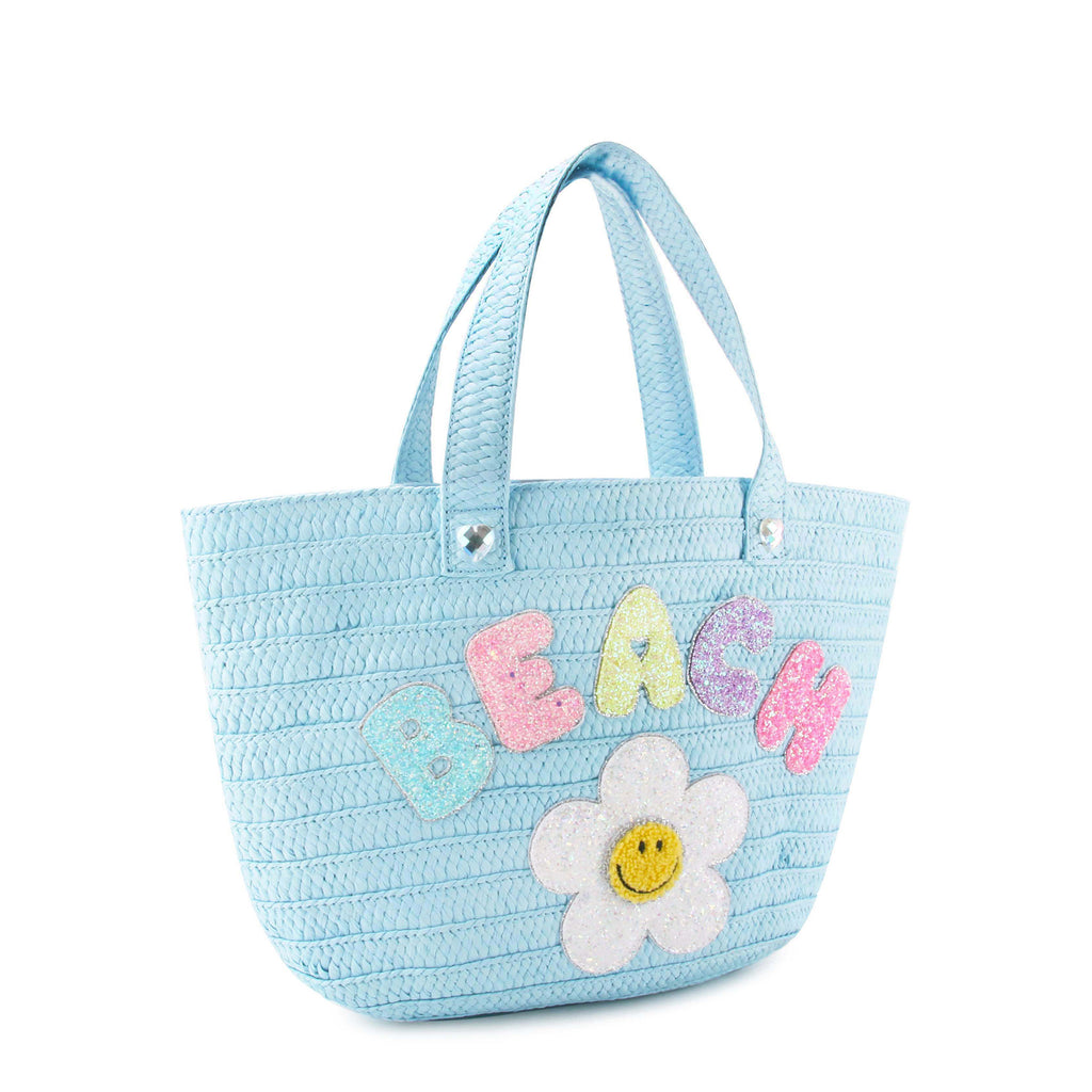 Side view of a blue straw beach tote with glitter bubble letters 'BEACH' and daisy appliqué