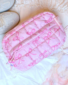 Photoshoot photo o a pink nylon quilted makeup pouch with a pink bow print, and beaded puller front zipper pocket