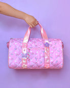 front view of a floral bow printed barrel duffle bag with butterfly & daisy appliques. pink metallic straps & beaded zipper pull