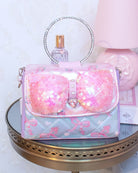 Lifestyle photo of a metallic color blocked mini bag with a round rhinestone handle and a large puffer sequins bow on the front flap