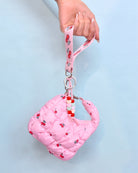 front view of a quilted pink cherry printed crescent shaped keychain and a pink cherry printed lanyard keychain with beaded detailing being held by lanyard strap