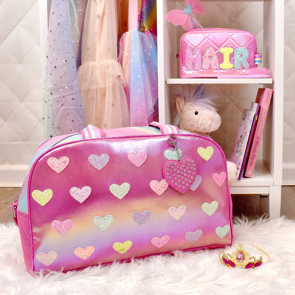 Lifestyle image of pink metallic heart-patched large duffle sitting in front of girl's wardrobe