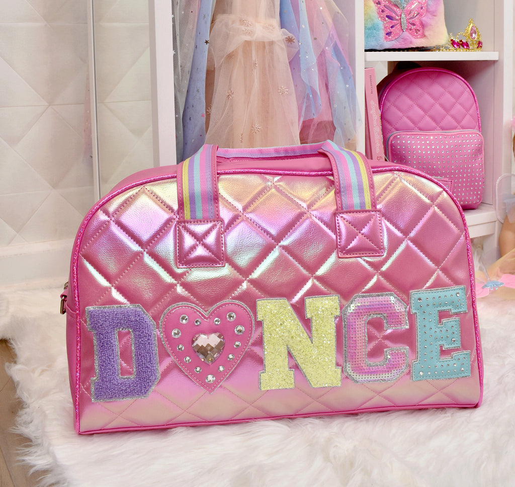 Lifestyle image of pink quilted metallic large 'Dance' duffle sitting in front of girl's wardrobe