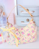 Photoshoot image of a floral yellow quilted bag with a pearl chain puller and bow bag charm