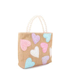 side view of a straw mini tote covered in glitter heart patches with a pearl handle