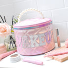 photoshoot photo of pink quilted metallic round train case with pearl handle and 'makeup' applique lettering