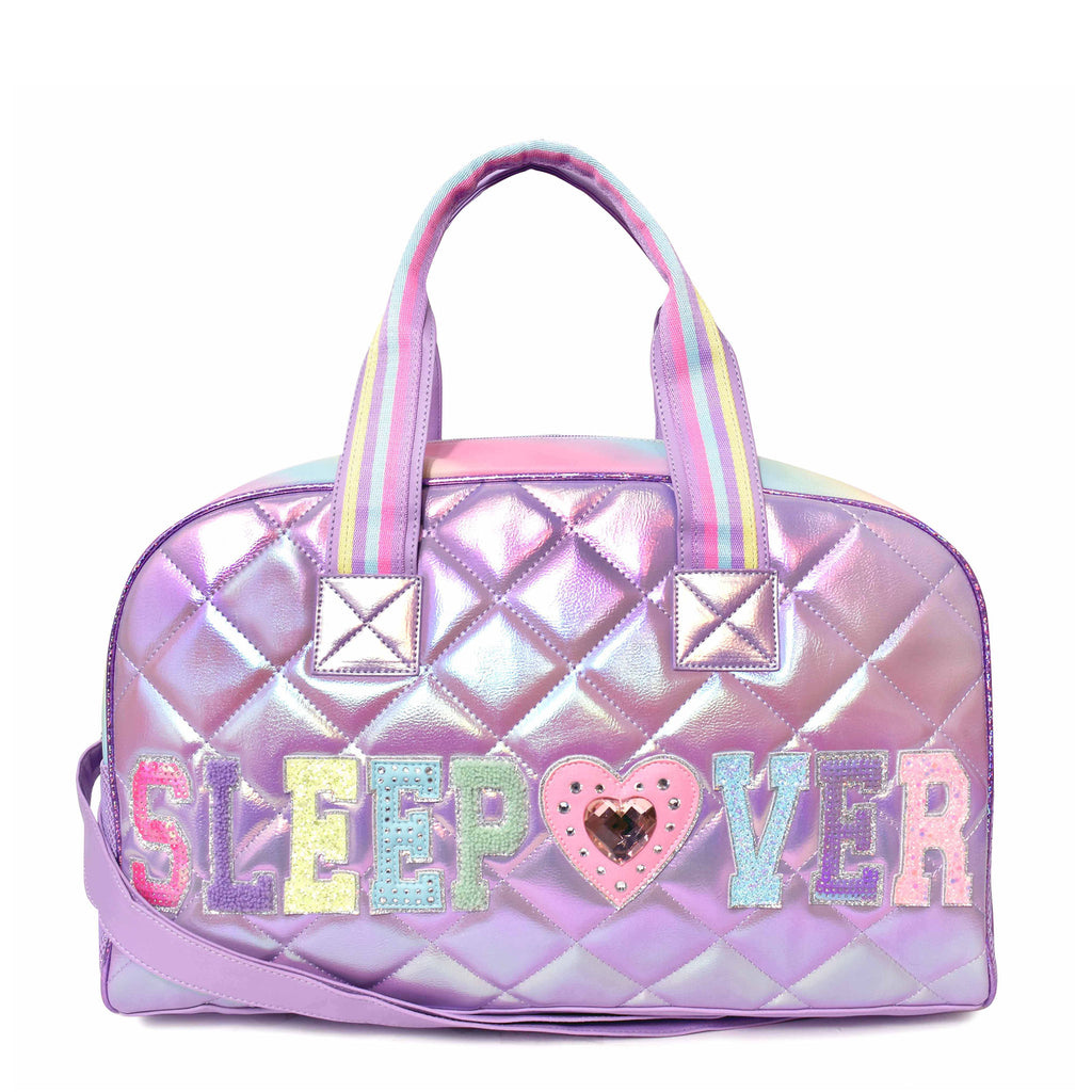 Front view of purple metallic medium 'Sleepover' duffle with multicolor varsity-letter patches and a rhinestone heart patch