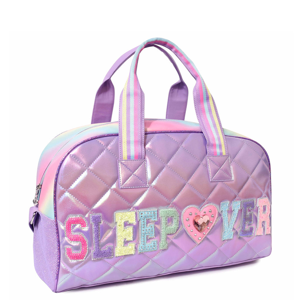 Side view of purple metallic medium 'Sleepover' duffle with multicolor varsity-letter patches and a rhinestone heart patch