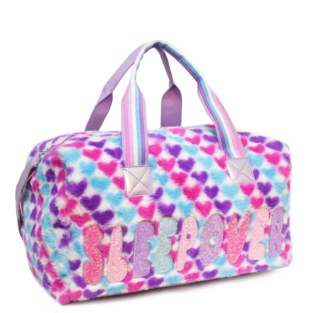 Side view of large plush multicolor heart-printed 'sleepover' duffle with glitter bubble-letter patches