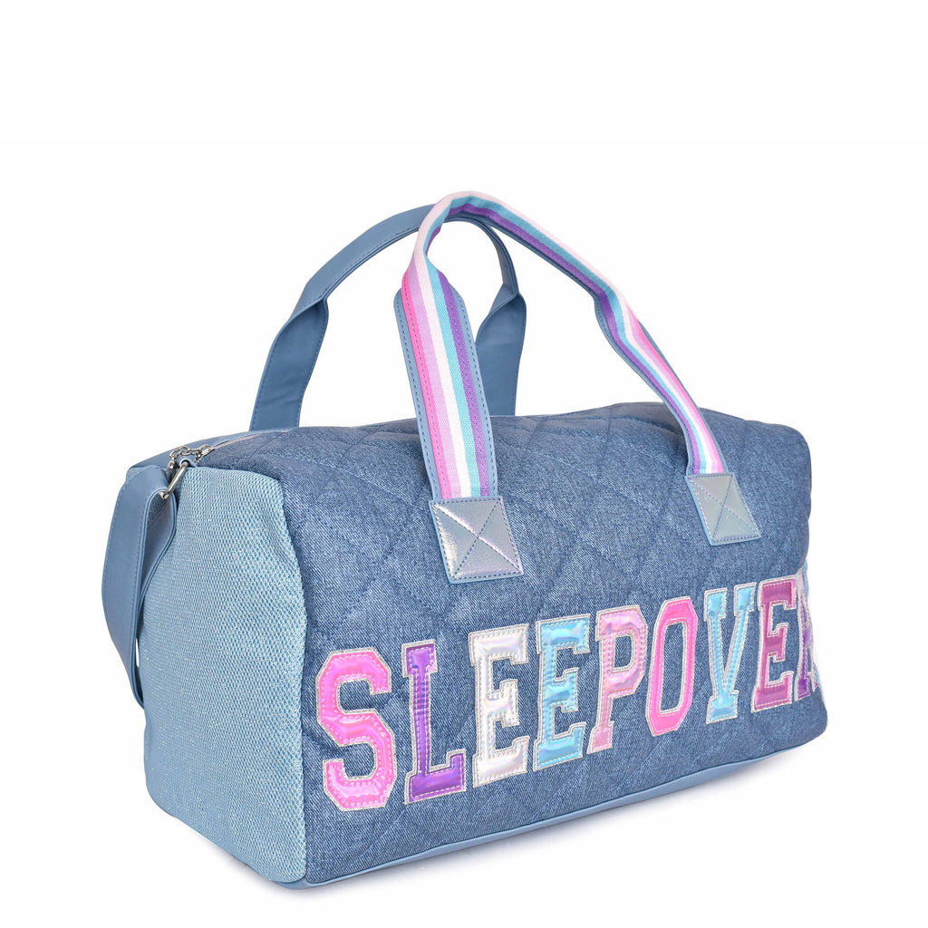 Side view of denim quilted large duffle bag with shoulder strap and metallic varsity letters 'SLEEPOVER'