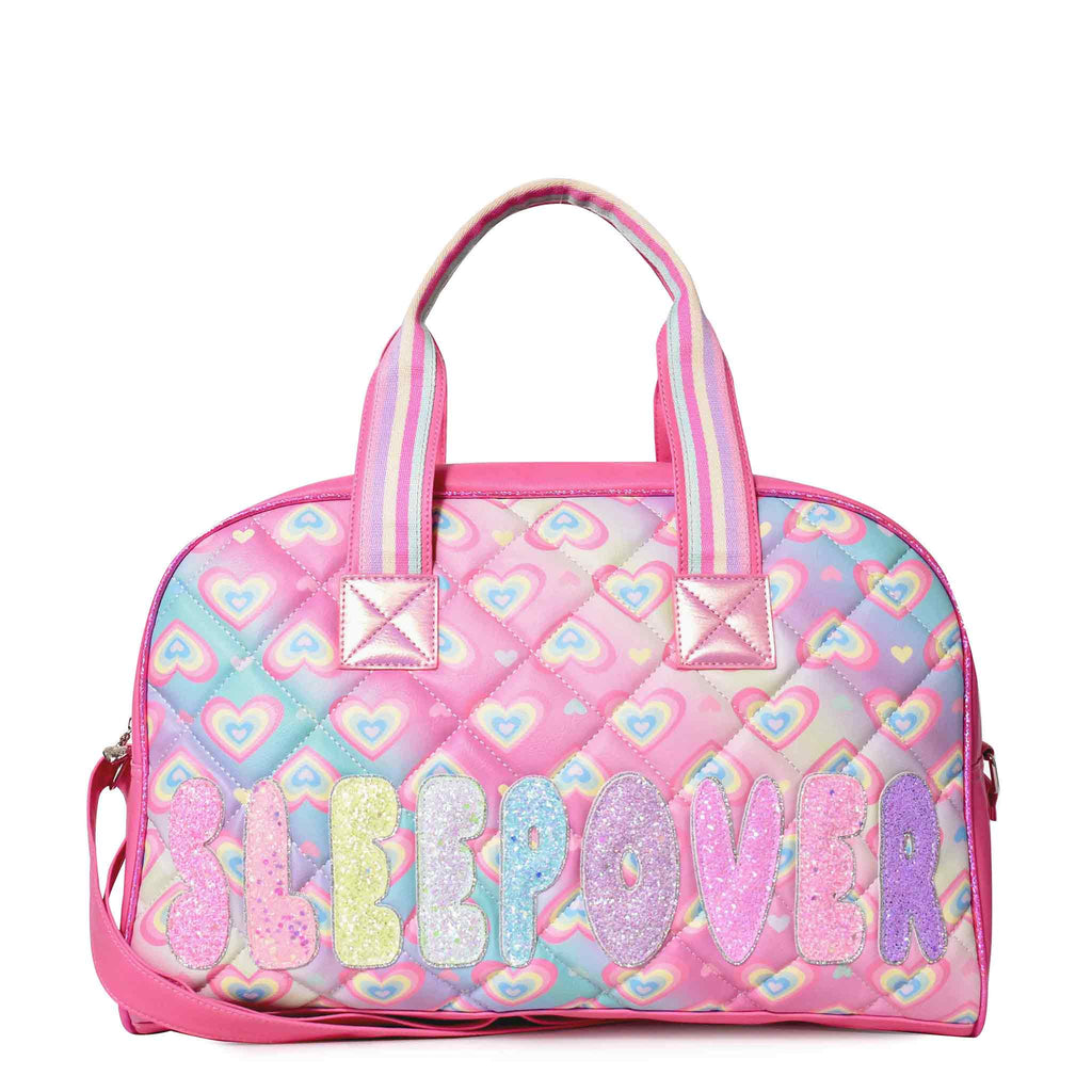 Front view of a Large quilted duffle covered in a heart print with glitter bubble-letters 'SLEEPOVER' appliqué
